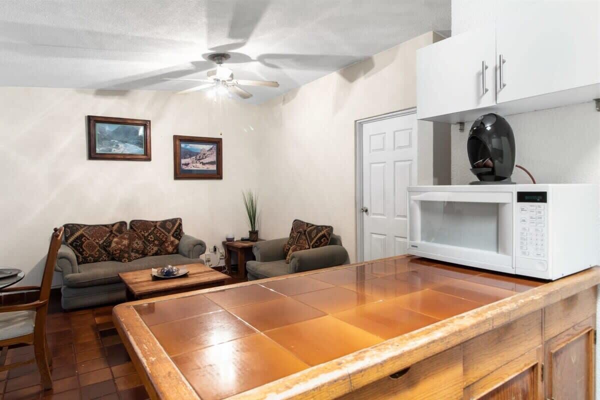 Una sala de estar con una mesa de centro de madera, dos sofás, un ventilador de techo y un microondas blanco sobre una encimera.