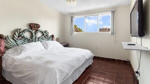 Un dormitorio con cama, ventilador de techo, ventana con vistas y televisor montado.