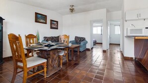 Comedor con mesa y sillas de madera, cocina con alacenas blancas y suelo de baldosas.