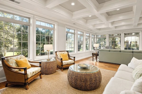A spacious living room with large windows, wicker furniture, and a green sofa.