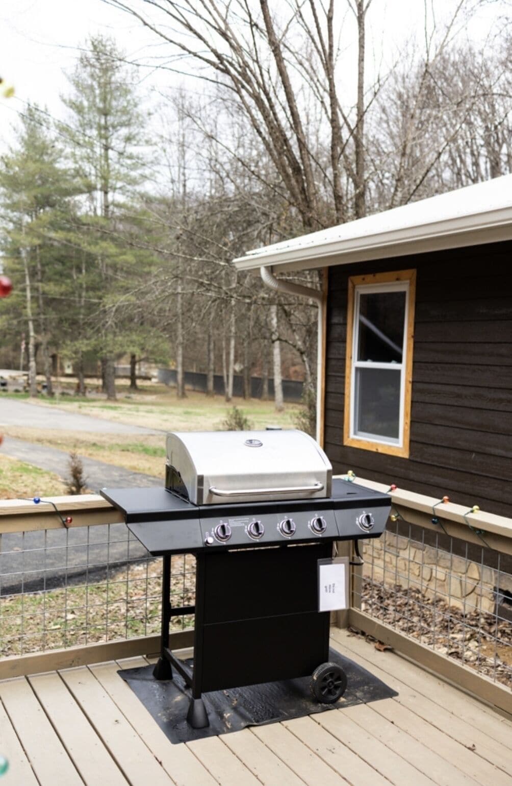 Una parrilla exterior en una terraza de madera con una casa al fondo.