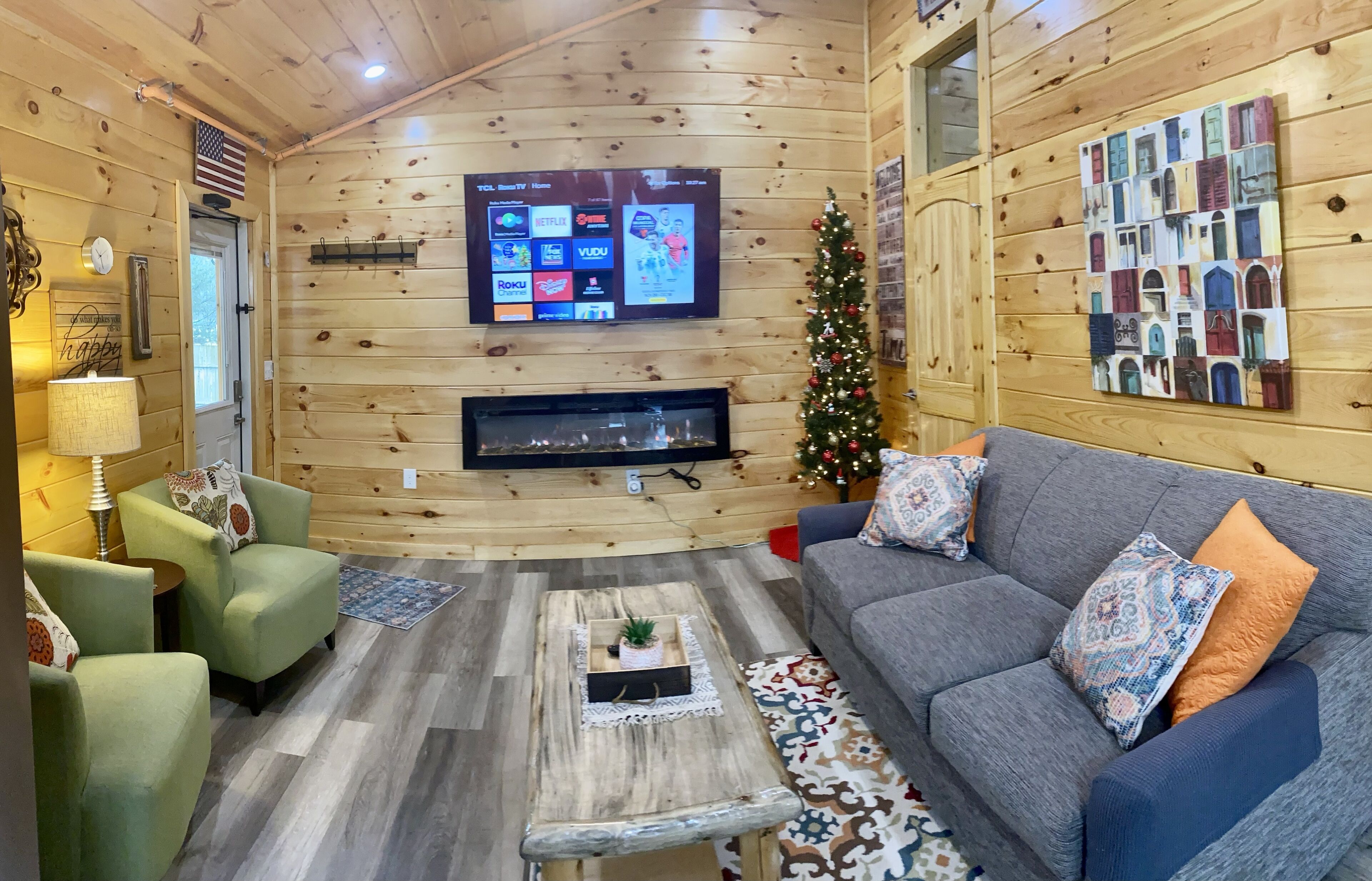A cozy log cabin interior with a fireplace, a television displaying streaming services, and a Christmas tree.