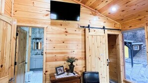 L’intérieur d’un chalet en bois est doté d’un téléviseur fixé au mur, d’une commode en bois, d’une chaise et d’une porte coulissante donnant sur un balcon.