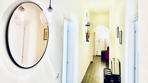 Um corredor com um espelho redondo, duas luminárias pendentes e uma porta que dá para outro cômodo.