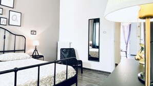 Quarto de hotel com cama, mesa de cabeceira, abajur, cadeira e espelho.