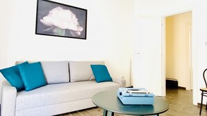 Uma sala de estar com um sofá cinza, almofadas verde-água, uma obra de arte com flores emolduradas e uma pequena mesa com uma caixa azul.