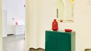 Um corredor com um armário verde, um vaso vermelho e um espelho na parede.
