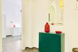 A hallway with a green cabinet, a red vase, and a mirror on the wall.