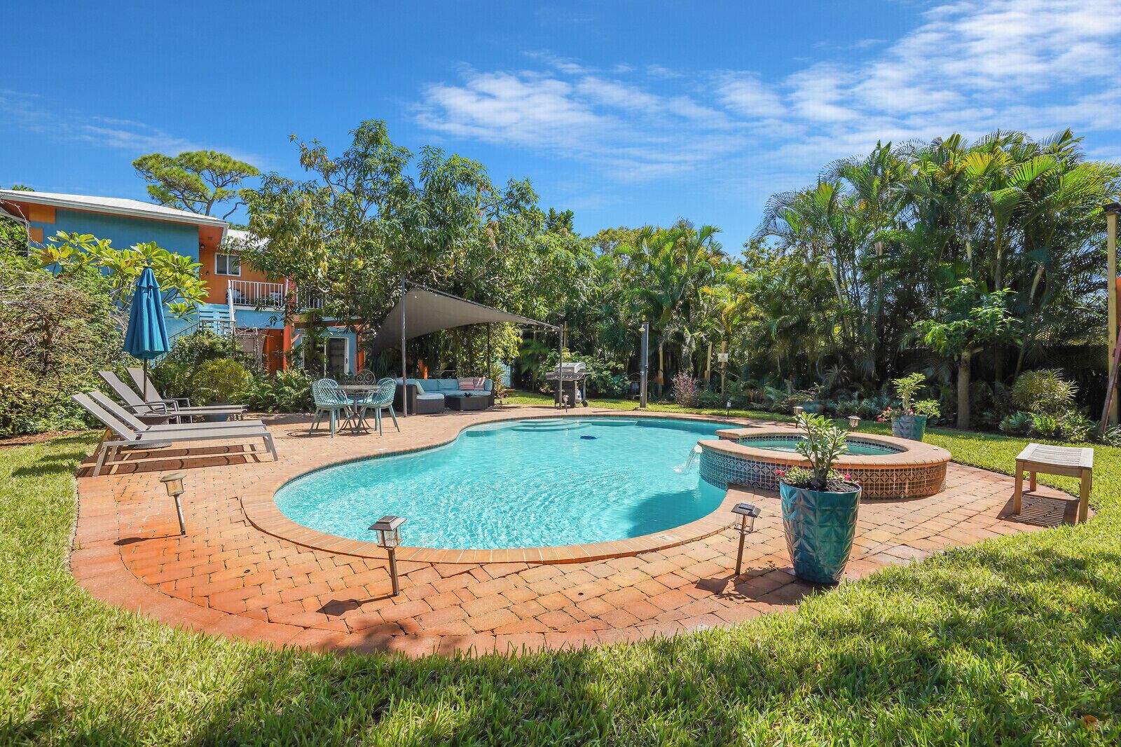 A swimming pool with a sunken hot tub, surrounded by a brick patio and lush greenery.