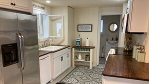 A kitchen with white cabinets, a stainless steel refrigerator, a sink, a coffee machine, and a sign that reads "BAKERY".