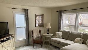 A living room with a television, a chair, a sofa, a small table with a lamp, and a framed picture on the wall.