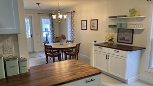 A kitchen with a wooden countertop, white cabinets, a chandelier, and a dining area with a table and chairs.