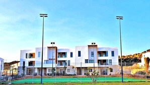 Ein modernes, mehrgeschossiges Wohngebäude mit flachem Dach, mehreren Balkonen und einem begrünten Sportplatz im Vordergrund.
