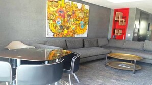 A modern living room with a gray sectional sofa, a round coffee table, and a dining table with chairs. A large abstract painting adorns the wall. - Residence Tamourrit Taghazout Bay 4747 (Taghazout)