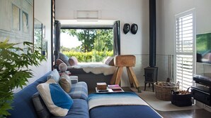 A cozy living room with a sofa, a fireplace, and a view of greenery outside. - Harts Lane Stag and Millies- sleek design and pet friendly (Daylesford)