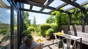 A covered patio with a table and chairs, surrounded by potted plants and a view of the landscape. - Harts Lane Stag and Millies- sleek design and pet friendly (Daylesford)