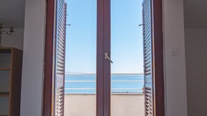 Una habitación con cama, un edredón de temática náutica, vista al mar a través de una puerta abierta y un balcón con barandilla.