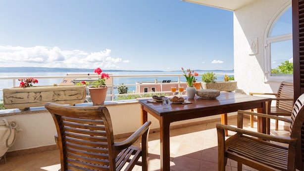 Una mesa y sillas de madera en un balcón con vista al mar.