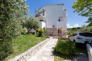 A two-story building with a stone pathway leading to the entrance, surrounded by greenery.