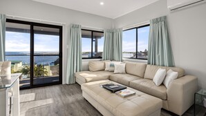 A modern living room with a beige sectional sofa, a glass coffee table, and a view of the sea through large windows. - UNIT 2  OPPOSITE BEACH, RIVER ,HOTEL,CLUB,WALKING DISTANCE TO ALL VENUES ETC..
 (HARRINGTON)