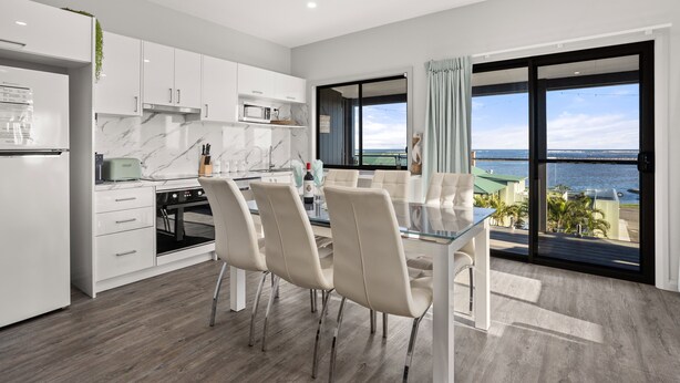 A modern kitchen with white cabinets, a marble backsplash, and a dining area with a glass table and chairs. - UNIT 2  OPPOSITE BEACH, RIVER ,HOTEL,CLUB,WALKING DISTANCE TO ALL VENUES ETC..
 (HARRINGTON)