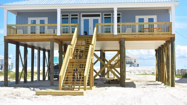 Una casa de playa de dos pisos con un balcón de madera y una escalera que lleva al nivel superior.