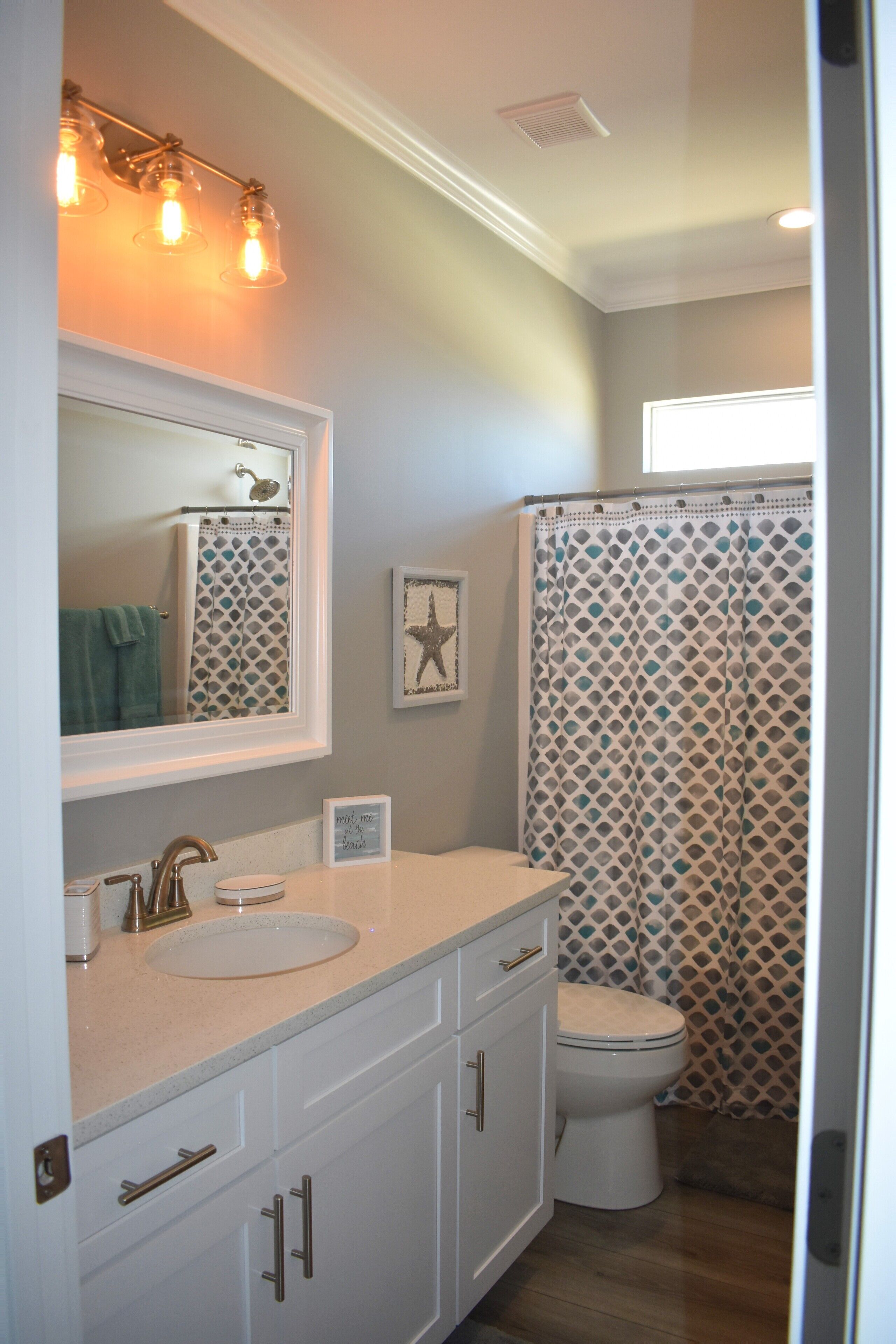 A bathroom with a white sink, vanity, and toilet. There is a shower curtain with a geometric pattern and a starfish decoration on the wall.