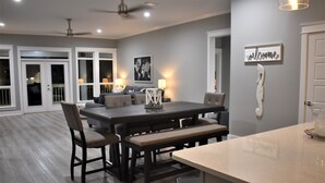 Cocina moderna con isla central, comedor con sillas y bancos, y vista al patio trasero a través de puertas de vidrio.