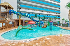 A swimming pool with a water slide, palm trees, and a multi-story building in the background. - WOW CORNER ALL GLASS PARLOR UNIT/60 FOOT OF BALCONY/2 BALCONIES (Myrtle Beach)