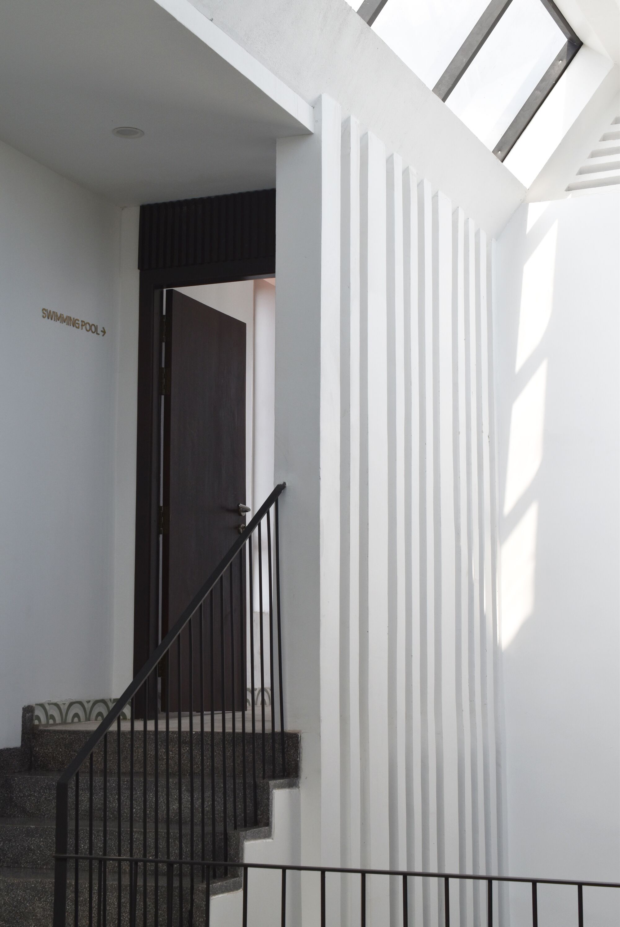 Eine Treppe mit schwarzer Geländer zum dunklen Türschild 'SWIMMING POOL'.