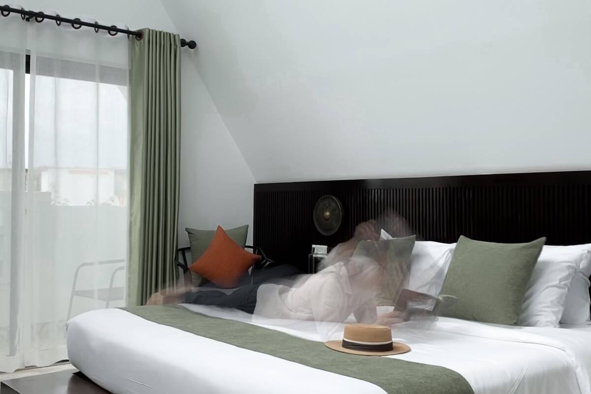 A modern bedroom with a large bed, a bedside table, a chair, and a window with curtains.