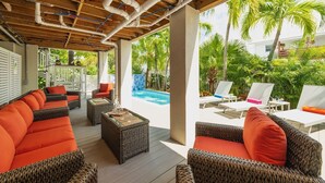 Un espace extérieur abrité, aménagé avec des meubles en osier, une piscine et une végétation luxuriante.