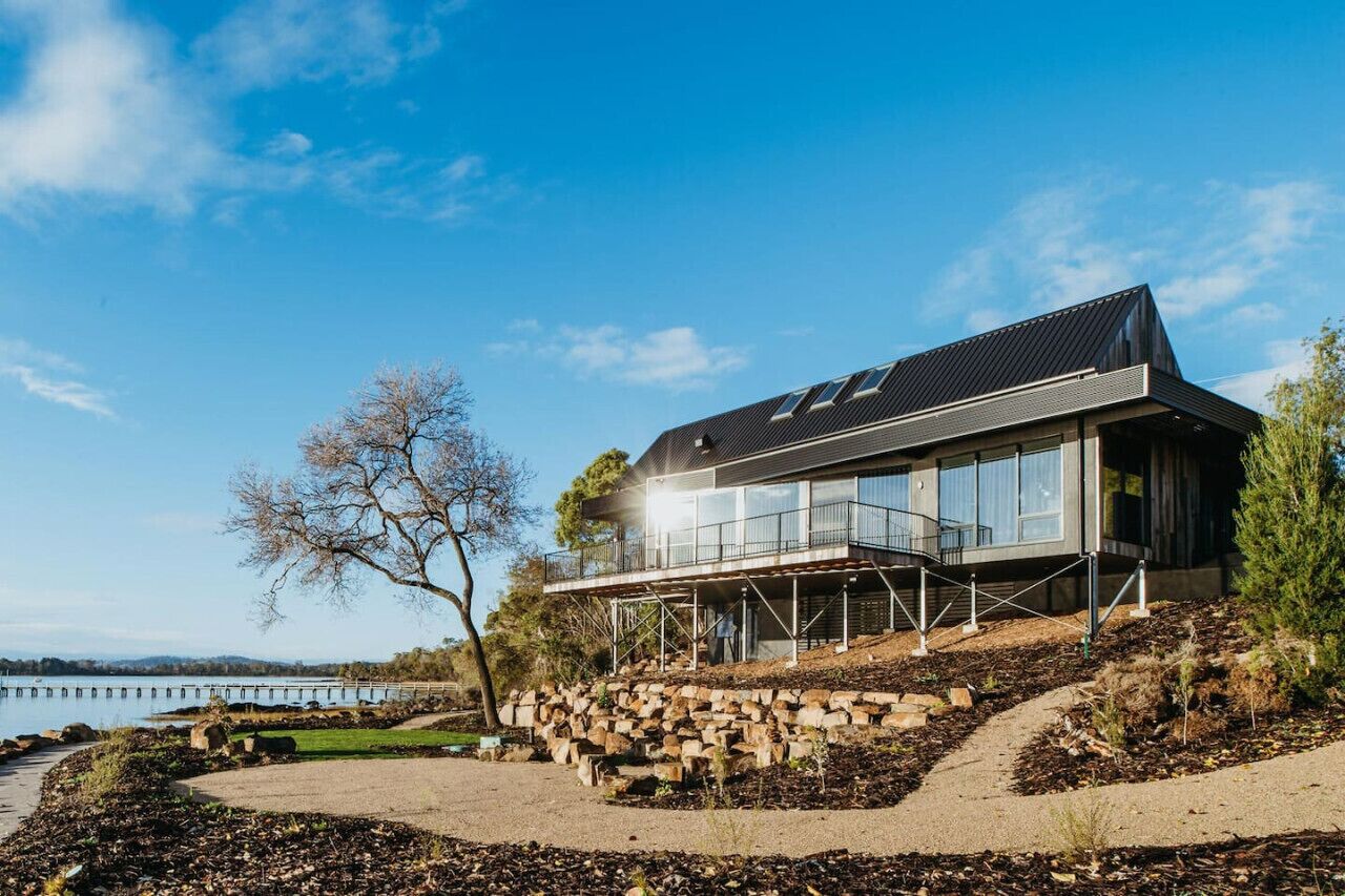 Ein modernes Haus mit Balkon, gelegen an einem Hang mit Blick auf das Wasser.