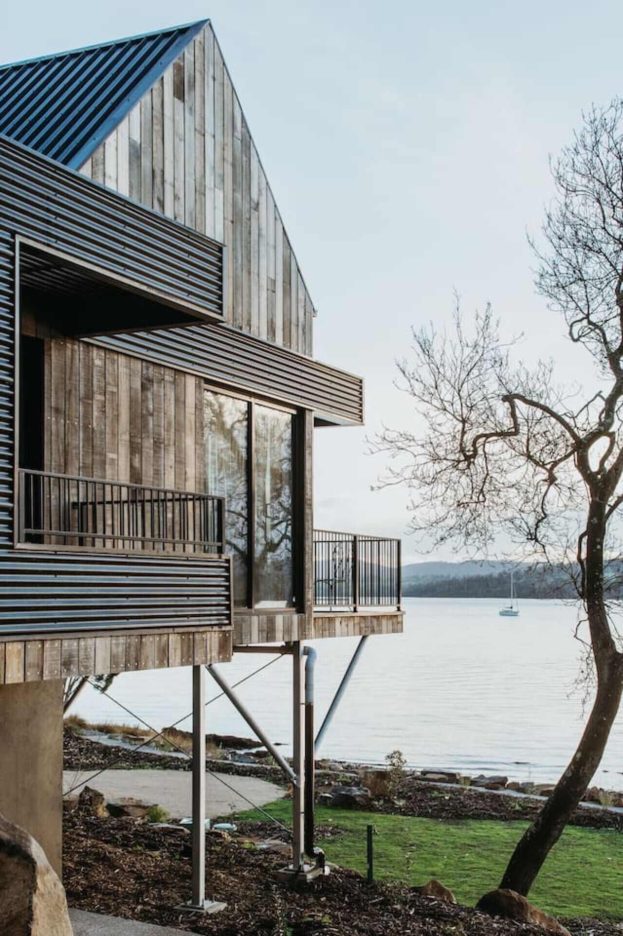 A modern wooden house with a balcony overlooking a lake.
