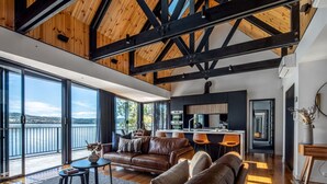 A spacious living area with a large window overlooking a body of water, a modern kitchen, and a cozy seating area with leather sofas. - Deviot Boat House - romantic, absolute waterfront (Deviot)