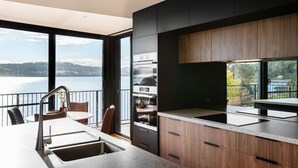 A modern kitchen with a large window overlooking a body of water, a built-in oven, and a dining area with a view. - Deviot Boat House - romantic, absolute waterfront (Deviot)