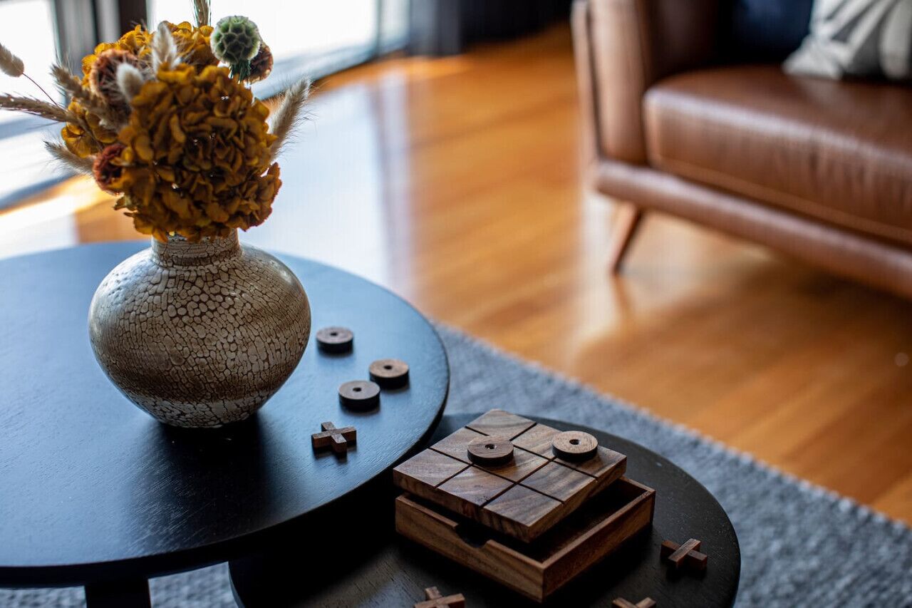 Una mesa redonda de madera con un jarrón de flores secas y un juego de madera.