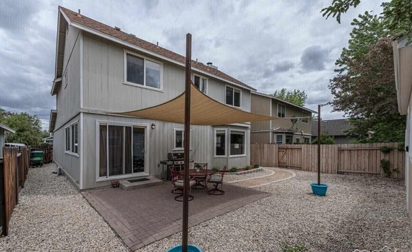 A two-story house with a patio area, a barbecue grill, and a table with chairs.