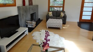 Ein Wohnzimmer mit Flachbildfernseher, Kamin, Sofa und Couchtisch mit Blumen.