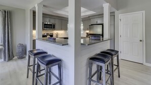 A modern kitchen with a central island, stainless steel appliances, and bar stools. - Sunset Rentals | Evian 233 (Hilton Head Island)