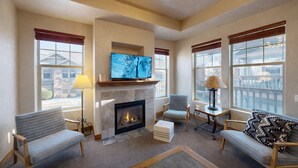 A spacious living room with a fireplace, comfortable seating, a television, and large windows offering a view of the outside. - Foxpoint 2 Bedroom Condo by RedAwning (Park City)
