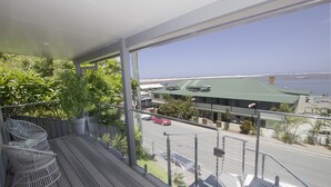 A balcony with wicker chairs, a view of the street, and a building with a green roof. - UNIT   1.. OPPOSITE THE OCEAN.. BEACH ..RIVER..PET FRIENDLY. 1 FREE PARKING  
 
 (HARRINGTON)
