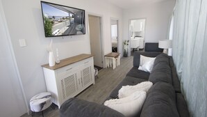A modern living room with a grey sofa, a white cabinet, and a flat-screen TV mounted on the wall. - UNIT   1.. OPPOSITE THE OCEAN.. BEACH ..RIVER..PET FRIENDLY. 1 FREE PARKING  
 
 (HARRINGTON)