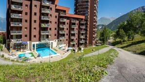 A modern multi-story hotel with balconies, a swimming pool, and a mountain backdrop. - Les Terrasses du Corbier by Interhome (Le Corbier)
