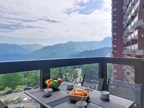 A balcony with a table set for breakfast, a fruit bowl, and a view of mountains. - Les Terrasses du Corbier by Interhome (Le Corbier)
