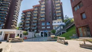 A multi-story residential building with balconies, a central courtyard, and an adjacent smaller building. - Les Terrasses du Corbier by Interhome (Le Corbier)