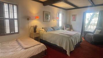 A bedroom with a bed, a smaller bed, a nightstand, a chair, and a window with blinds.