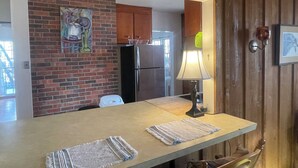 A kitchen with a brick wall, a refrigerator, a wooden cabinet, and a hanging light fixture. - Funky and Charming Home! (Laramie)