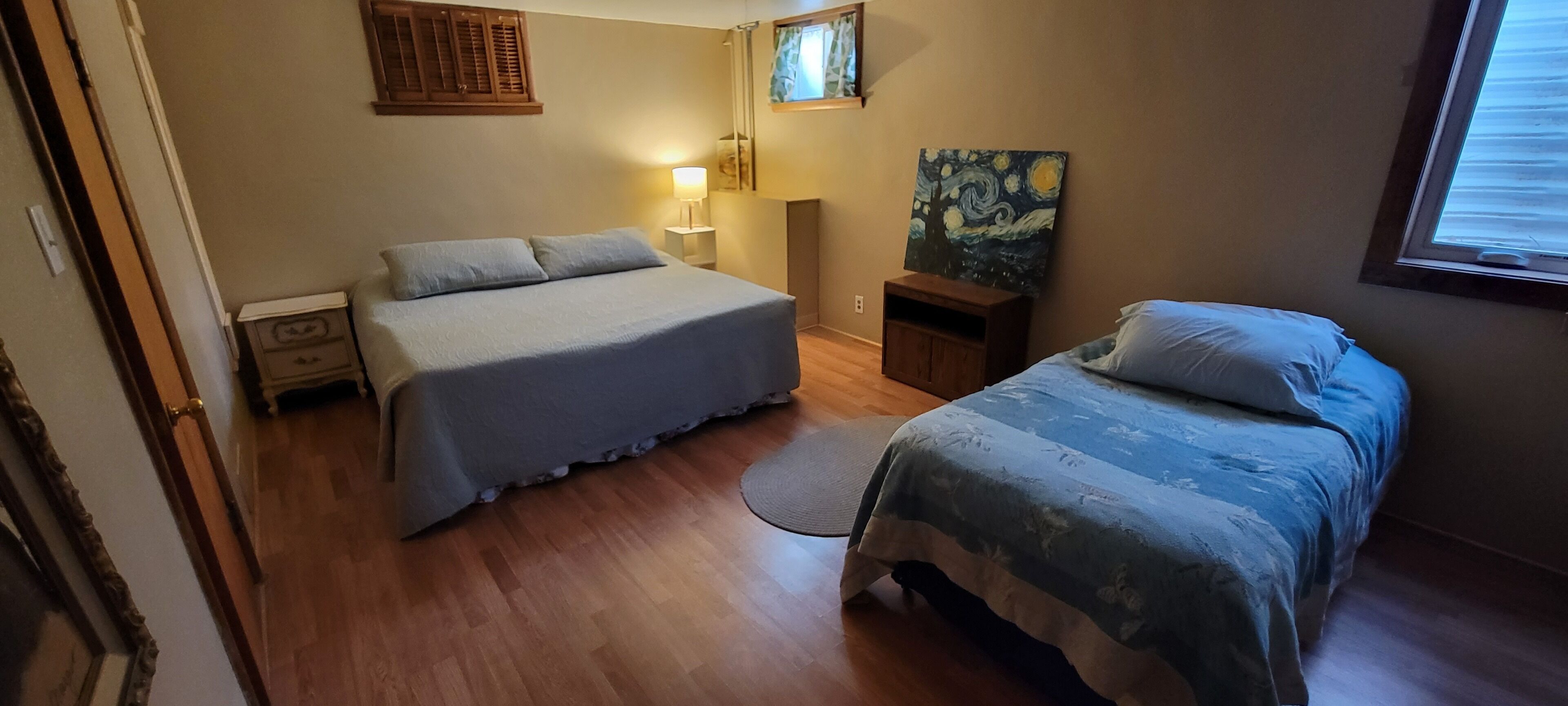 Een slaapkamer met twee bedden, een nachtkastje, een lamp en een schilderij aan de muur.
