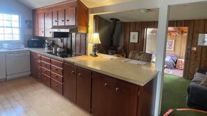 A kitchen with wooden cabinets, a microwave, and a stove. There is a dining area with a table and chairs. - Funky and Charming Home! (Laramie)